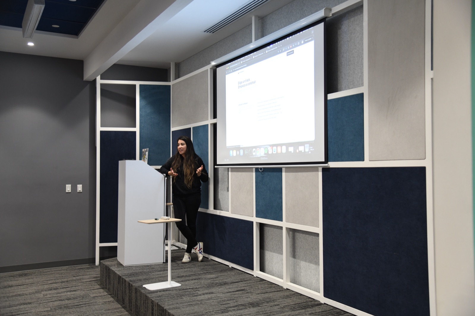 Aileen presenting beside a lectern, gesturing as she explains a projected demo